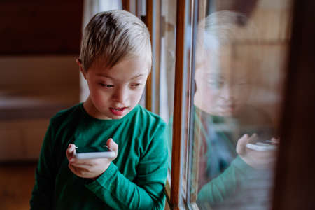 Sad little boy with Down syndrome using smartphone at home