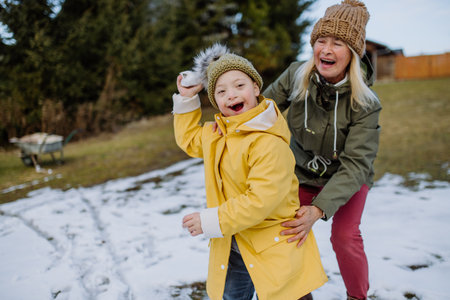 Boy with Down syndrome with his mother playing with snow in garden.の写真素材