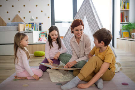 Cheerful mother of three little children reading them book at home.の写真素材