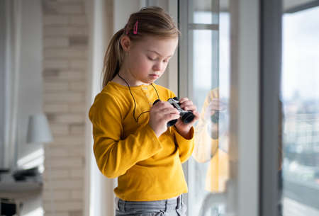 Curious little girl with Down syndrome with binoculars looking through on window at home.の写真素材