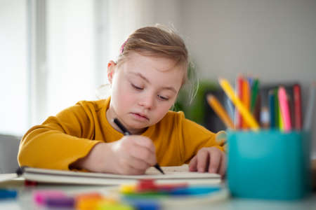 Little girl with Down syndrome drawing at home.