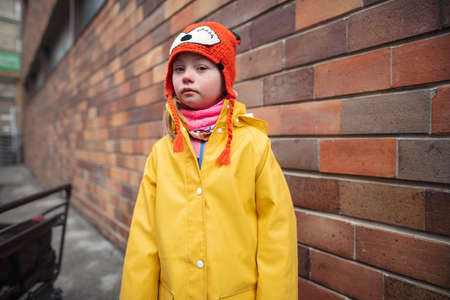 Little girl with Down syndrome looking at camera outoors in winter against brick wall.の写真素材