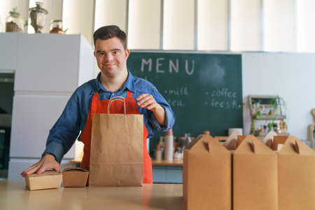 Cheerful young Down Syndrome waiter working in take away restaurant, social inclusion concept.