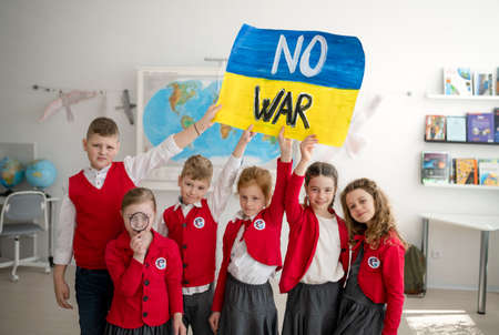 Little schoolchildren holidng and showing ukrainian flag in classroom, no war concept.