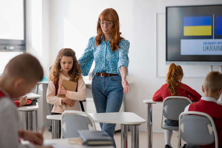 Teacher with Ukrainian schoolgirl in classroom, concept of enrolling Ukrainian kids to schools.の写真素材