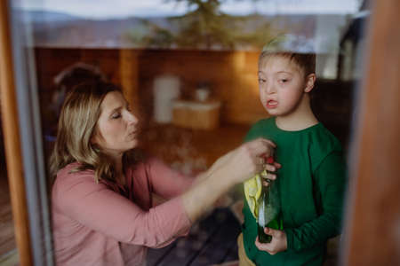 Boy with Down syndrome with his mother cleaning window at home.の写真素材