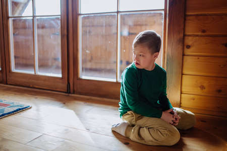 Sad little boy with Down syndrome sitting on floor at home.の写真素材