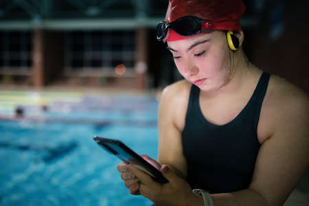 Young woman with Down syndrome in swimming pool using smartphoneの写真素材