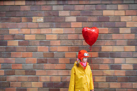 Little girl with Down syndrome holding heart shaped balloon in winter against brick wall.の写真素材