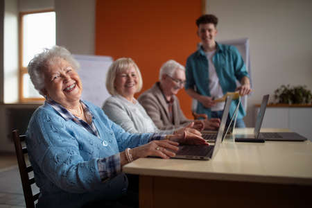 Senior group in retirement home with young instructor learning together in computer class