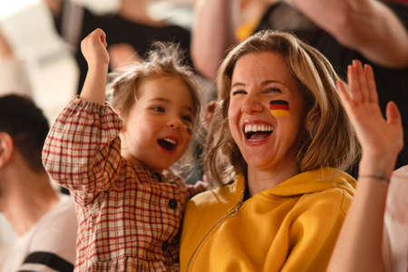 Excited football fans, mother with little daughter, supproting German national team in live soccer...