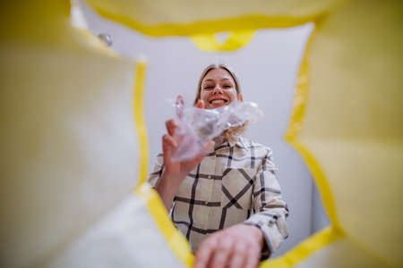 Image from inside yellow recycling bag of woman throwing a plastic bottle to recycle.