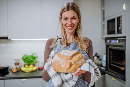 Happy woman holding homemade sourdough bread, cooking at home concept.の写真素材