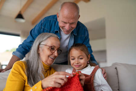 Little girl sitting on sofa with her grandparents and learning to knit indoors at home.の写真素材