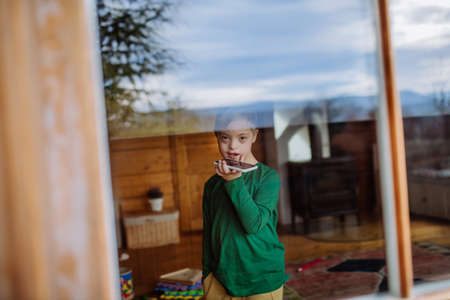 Sad little boy with Down syndrome using smartphone at home