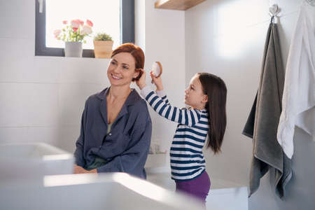 Little girl brushing her mothers hair in bathroom, morning routine concept.の写真素材