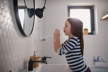 Little girl in bathroom, washing hands and doing bubbles from soap.