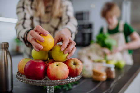 Mother unpacking shopping, vegetables and fruit, with help of daughter in kitchen at home.
