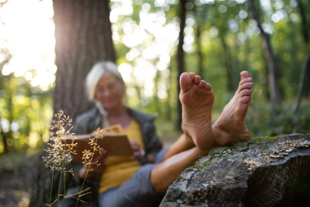 Senior woman relaxing and reading book outdoors in forest.の写真素材
