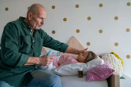 Grandfather taking care of his ill granddaughter lying in bed.の写真素材