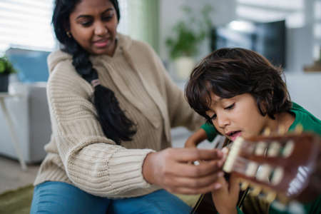 Little multiracial boy learning to play the guitar with his mother at home.の写真素材