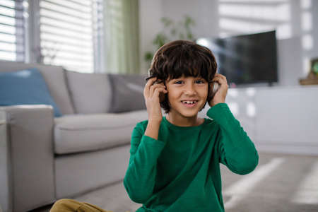 Happy multiracial boy with headphones listening to music at home.の写真素材