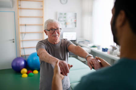Young physiotherapist exercising with senior patient in a physic roomの写真素材