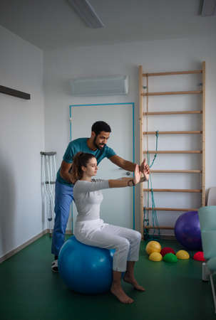 Young male physiotherapist exercising with young woman patient on ball in a physic roomの写真素材