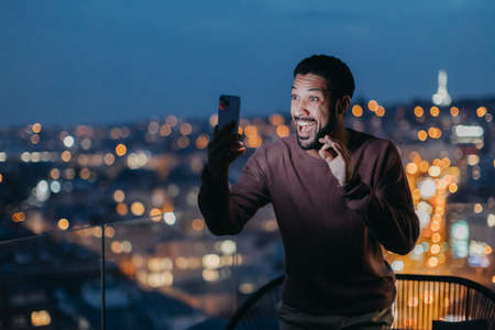 Cheerful young man taking selfie on balcony with urban view.の写真素材