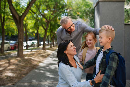 Happy grandparents taking grandchildren home from school, waiting in front of school outdoors in street.の写真素材