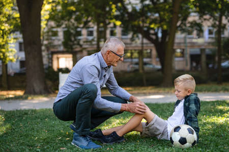 Little boy with injured leg getting plaster from grandfather outdoors in park.
