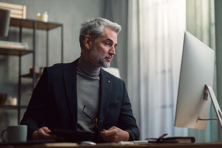 Mature businessman working on computer indoors in office.
