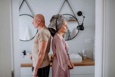 Senior couple in bathroom, standing back to back, relationship problems concept.