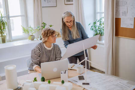 Mature women eco architects with blueprints working on lapotp together in office.の写真素材