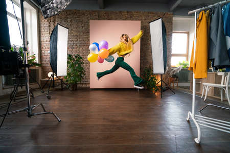 Fashion studio portrait of a happy young woman with balloons jumping, backstage of photoshooting .の写真素材