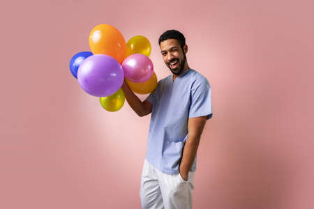 Happy young pediatrician holding balloons over pink backgroundの写真素材