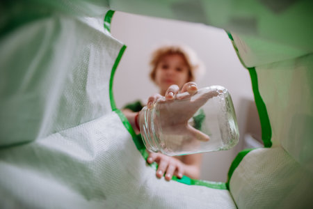 Image from inside green recycling bag of girl throwing a glass bottle to recycle.の写真素材