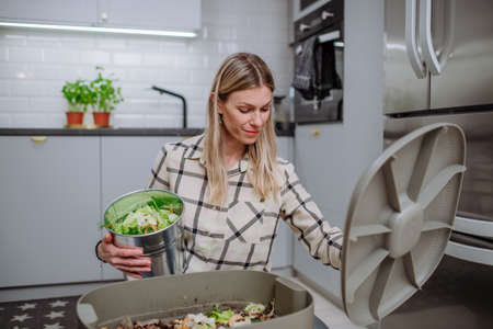 Woman throwing vegetable cuttings in a compost bucket in kitchen.の写真素材