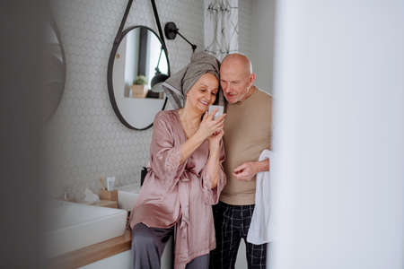 Senior couple in love in bathroom, using smartphone, morning routine concept.の写真素材