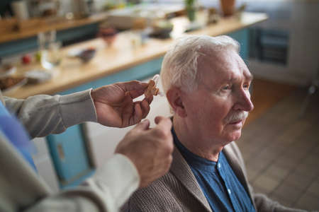 Caregiver helping senior man to insert hearing aid in his ear.の写真素材