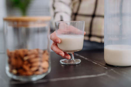 Unrecognizable woman holding glass with almond milk in kitchen. Healthy vegan product concept.