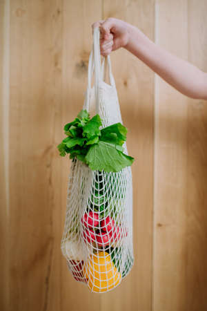 Woman holding a reusable mesh bag with fresh vegetables. Zero waste concept.の写真素材