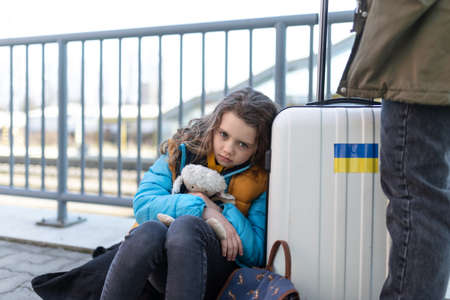 Sad Ukrainian immigrant child with luggage waiting at train station, Ukrainian war concept.の写真素材