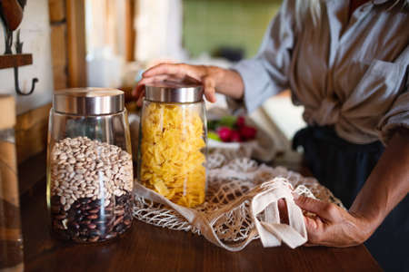 Close-up of senior woman unpacking local food in zero waste packaging from bag in kitchen at home.の写真素材