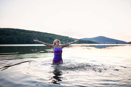 Portrait of active senior woman swimmer standing and stretching outdoors in lake.