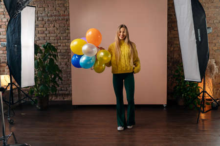 Studio portrait of a happy young blonde woman with balloons over pink background.