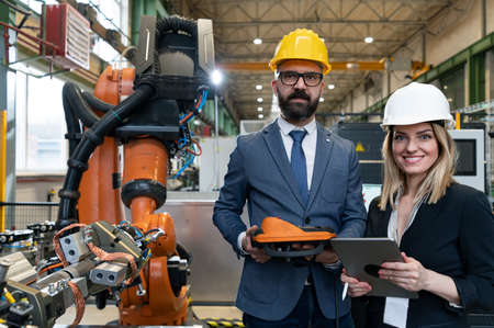 Chief engineer and project manager in modern industrial factory with robot arms talking and planning...