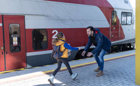 Happy Ukrainian refugee girl running to her father waiting at railway station, reunion after war.