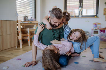 Cheerful father with three little daughters playing together at home.の写真素材