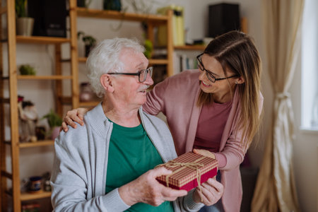 Happy woman surprising her senior father when visiting him at home and bringing present.の写真素材